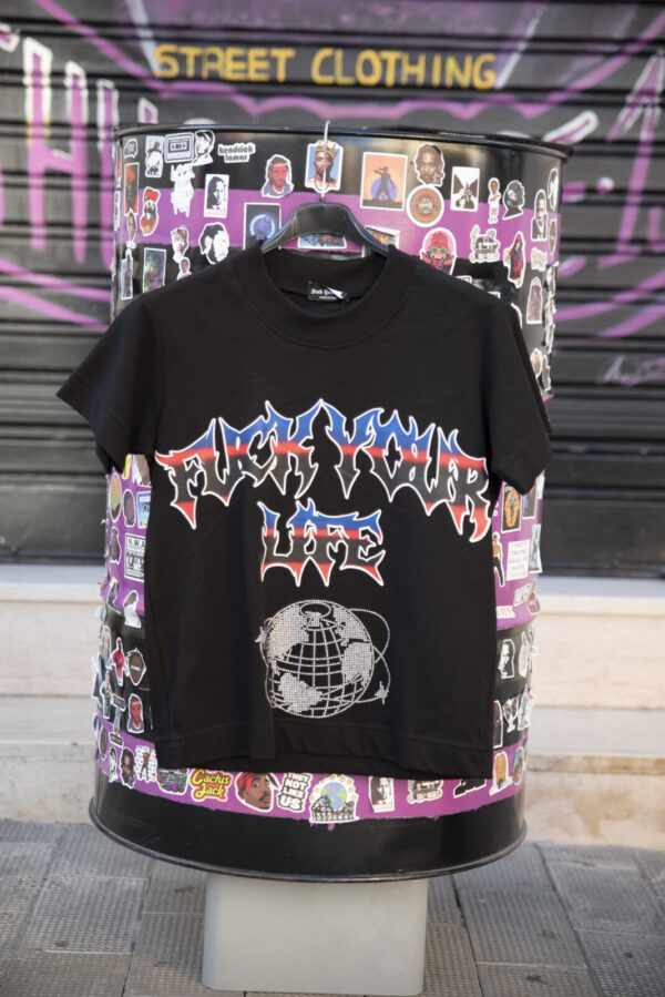 Maglietta nera con scritta "Fuck Your Life" in stile streetwear su sfondo di adesivi colorati.