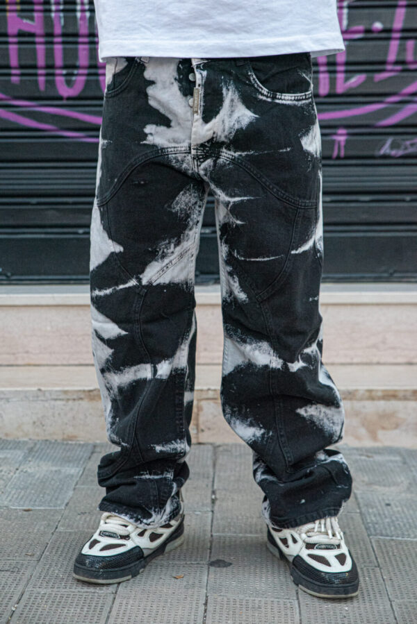 Pantaloni baggy neri effetto tie-dye bianco con scarpe sportive bianche e nere in un contesto urbano.
