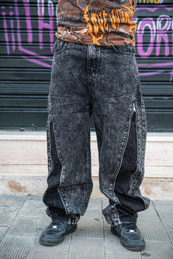 Jeans neri effetto lavato con zip e strass, abbinati a una maglietta grafica arancione e scarpe sportive nere.