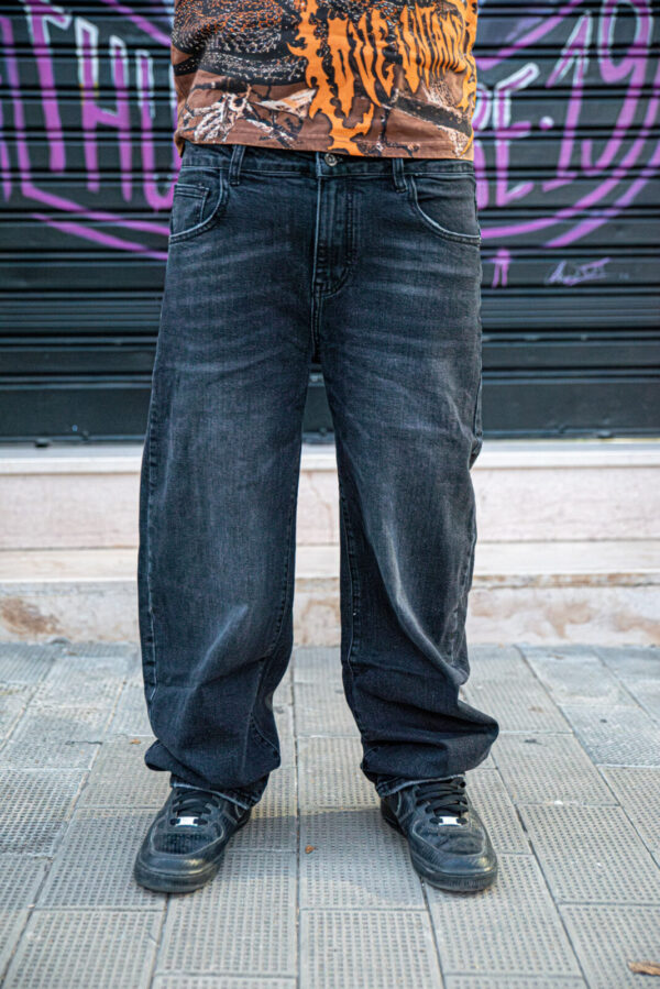 Jeans neri baggy abbinati a scarpe sportive nere e maglietta grafica su sfondo urbano.