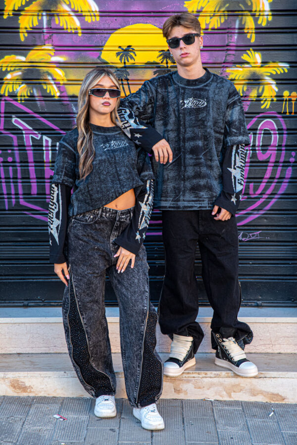Giovani con occhiali da sole indossano abbigliamento streetwear nero davanti a un murale colorato con palme e sole al tramonto.
