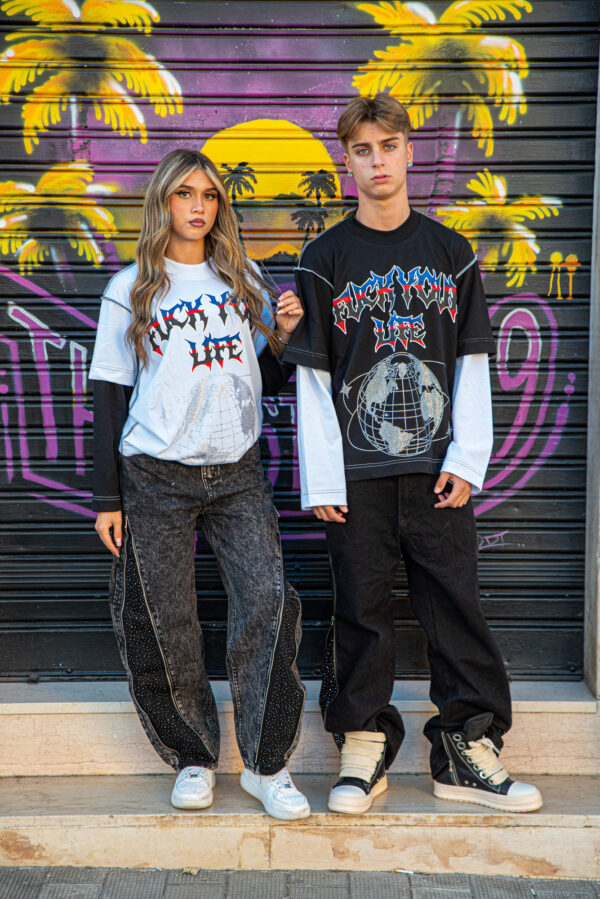 Giovani in abbigliamento streetwear con t-shirt grafiche e jeans larghi davanti a un murale colorato di palme e tramonto.