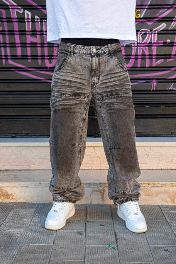 Jeans larghi grigi con effetto slavato abbinati a sneakers bianche e t-shirt bianca, davanti a una parete con graffiti.