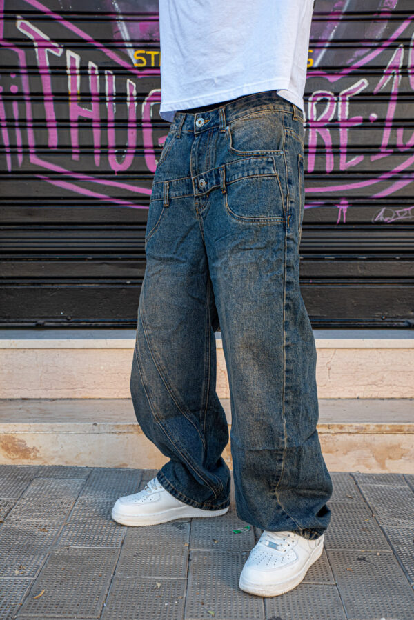 Jeans larghi in denim blu scuro abbinati a una maglietta bianca e scarpe da ginnastica bianche su sfondo urbano.