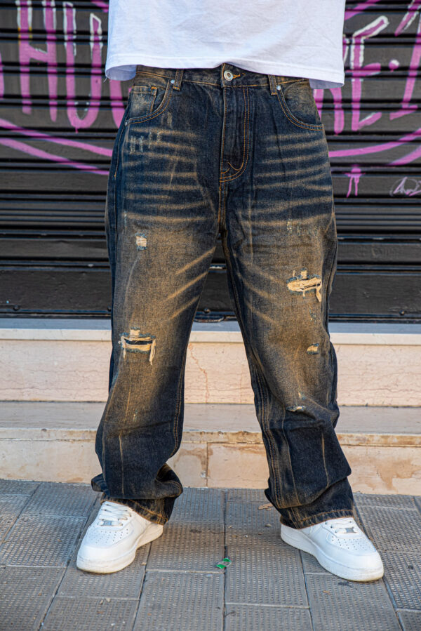 Jeans strappati blu scuro con effetto sbiadito indossati con sneakers bianche su sfondo urbano.
